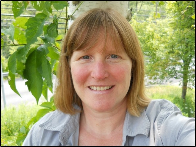 Woman with gray shirt in front of green leaves