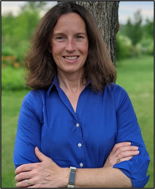 Woman in blue shirt in front of a tree.