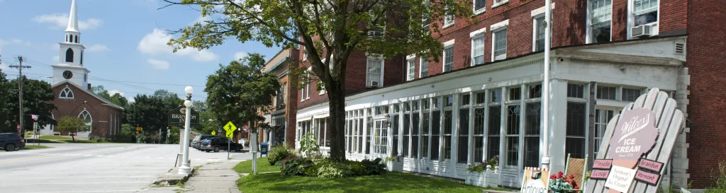 Red brick building on right side of frame with a tree in front of the building. A sidewalk and street run in front of the building