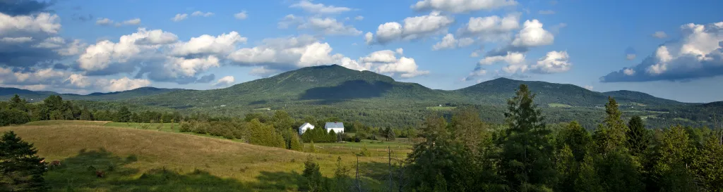 blue sky with clouds, rolling green hills and mountain in foreground